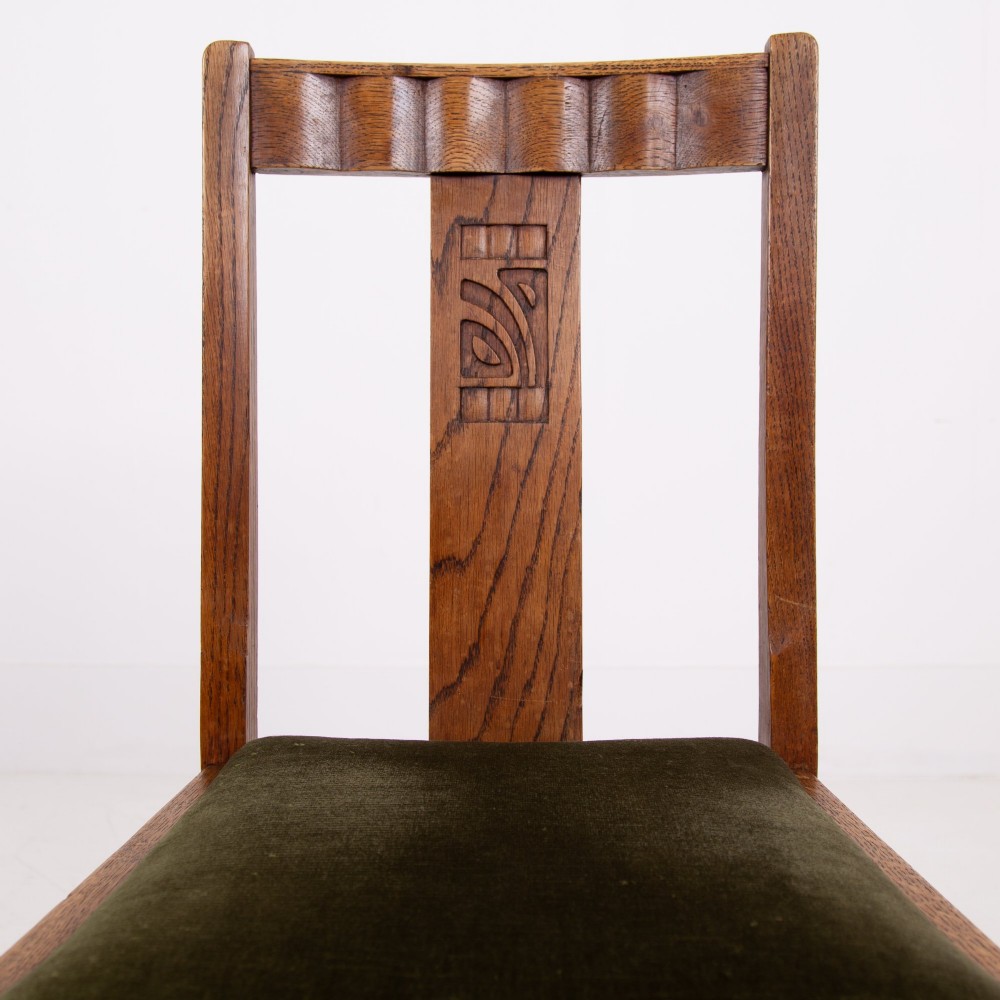 A set of four 1930s oak dining chairs featuring carved back splats, fluted top rails, and green velvet upholstered seats. View V