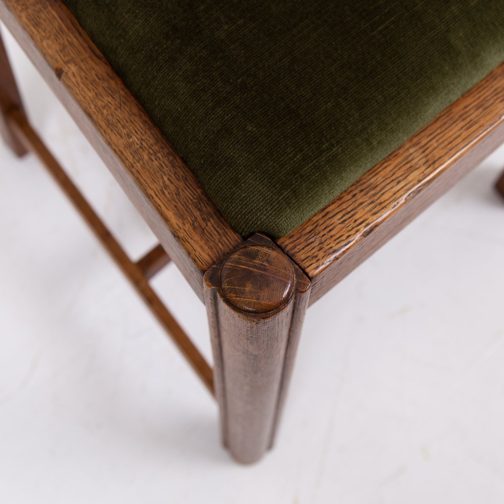 A set of four 1930s oak dining chairs featuring carved back splats, fluted top rails, and green velvet upholstered seats. View VI