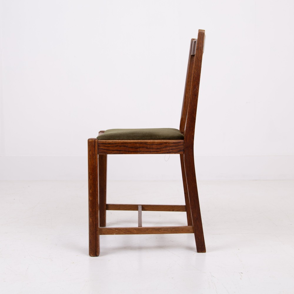A set of four 1930s oak dining chairs featuring carved back splats, fluted top rails, and green velvet upholstered seats. View X