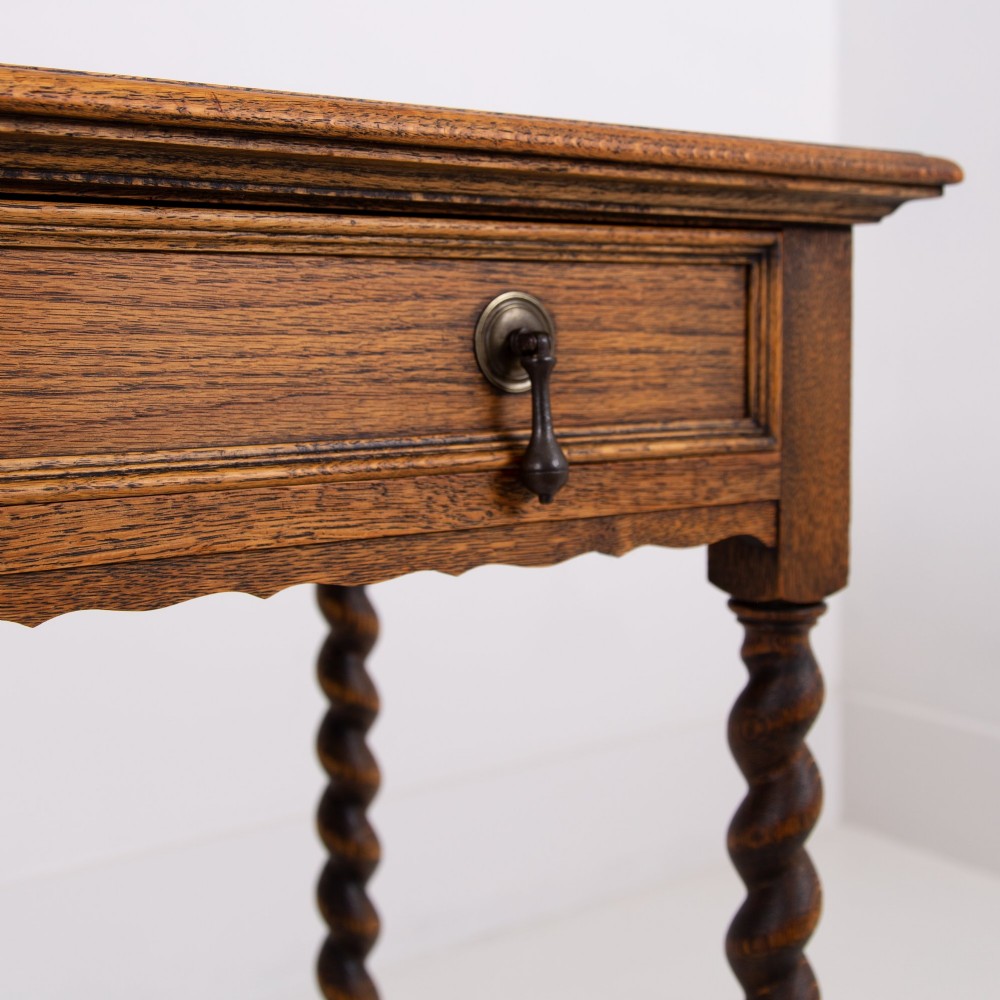 An antique English oak side table featuring a single drawer with metal drop handles, set upon four barley twist legs connected by an H-stretcher base. View VII