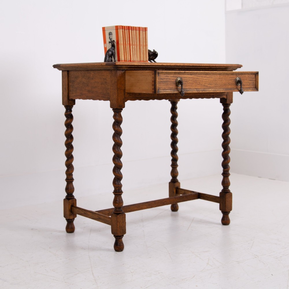 An antique English oak side table featuring a single drawer with metal drop handles, set upon four barley twist legs connected by an H-stretcher base. View X