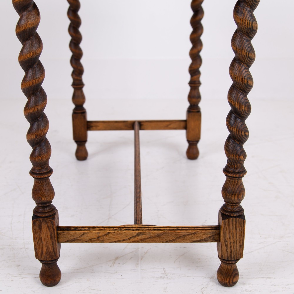 An antique English oak side table featuring a single drawer with metal drop handles, set upon four barley twist legs connected by an H-stretcher base. View XII