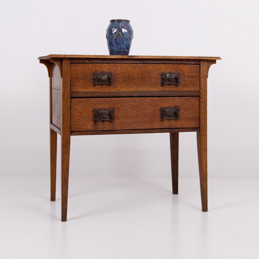 An early 20th-century oak side table with two drawers, decorative metal drop handles, and tapered square legs.
