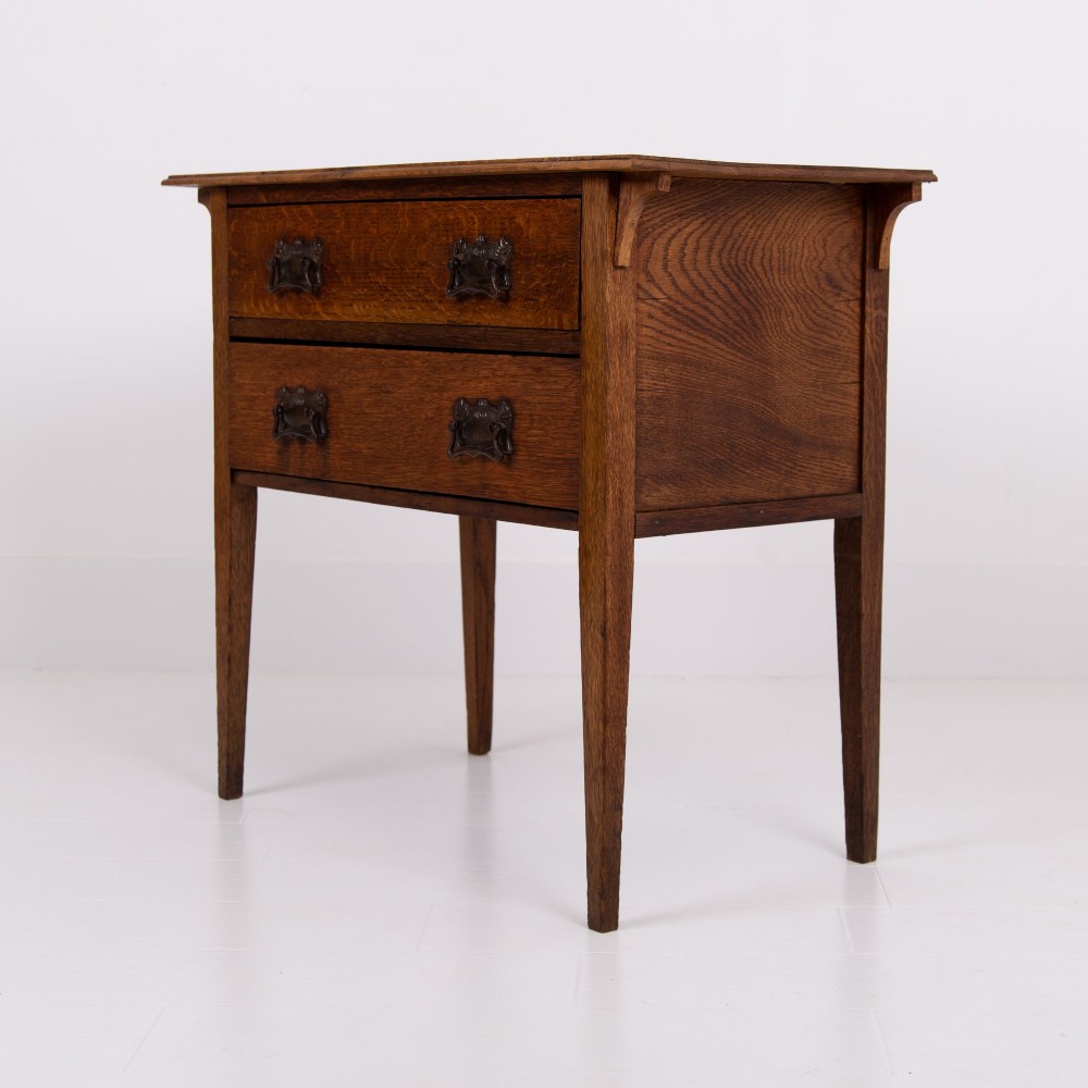 An early 20th-century oak side table with two drawers, decorative metal drop handles, and tapered square legs. View VI
