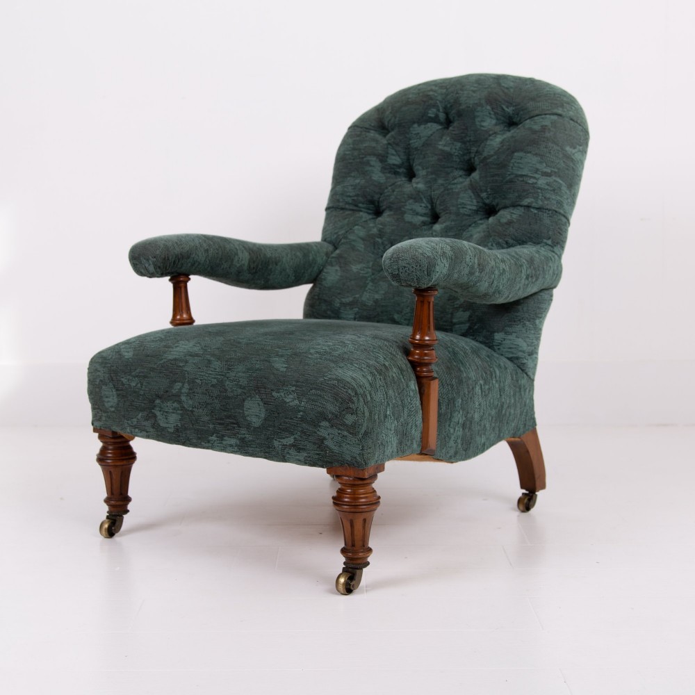 A profile view of a Victorian walnut open library armchair with dark green button-backed upholstery, turned front legs, and brass castors. View III