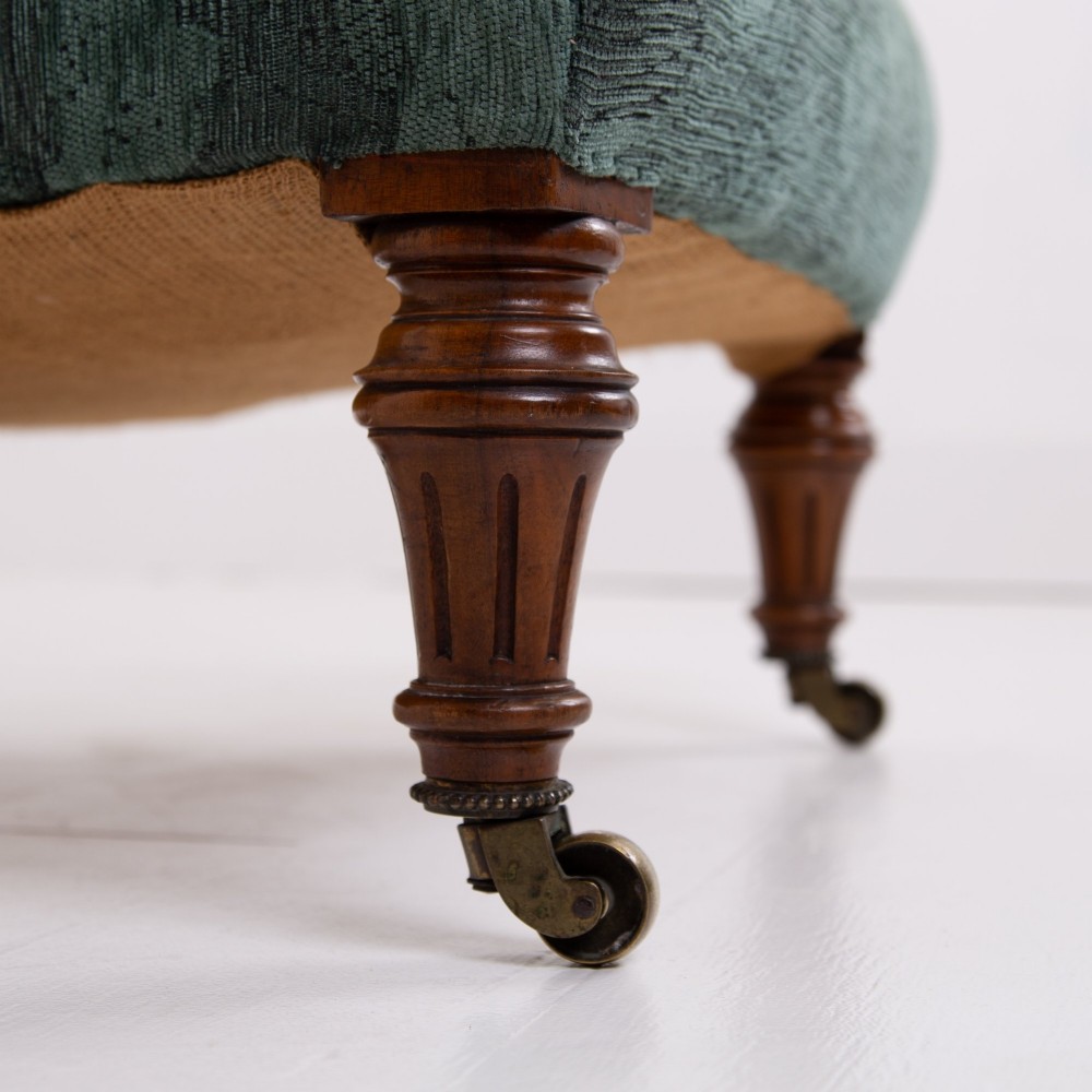 A profile view of a Victorian walnut open library armchair with dark green button-backed upholstery, turned front legs, and brass castors. View IV