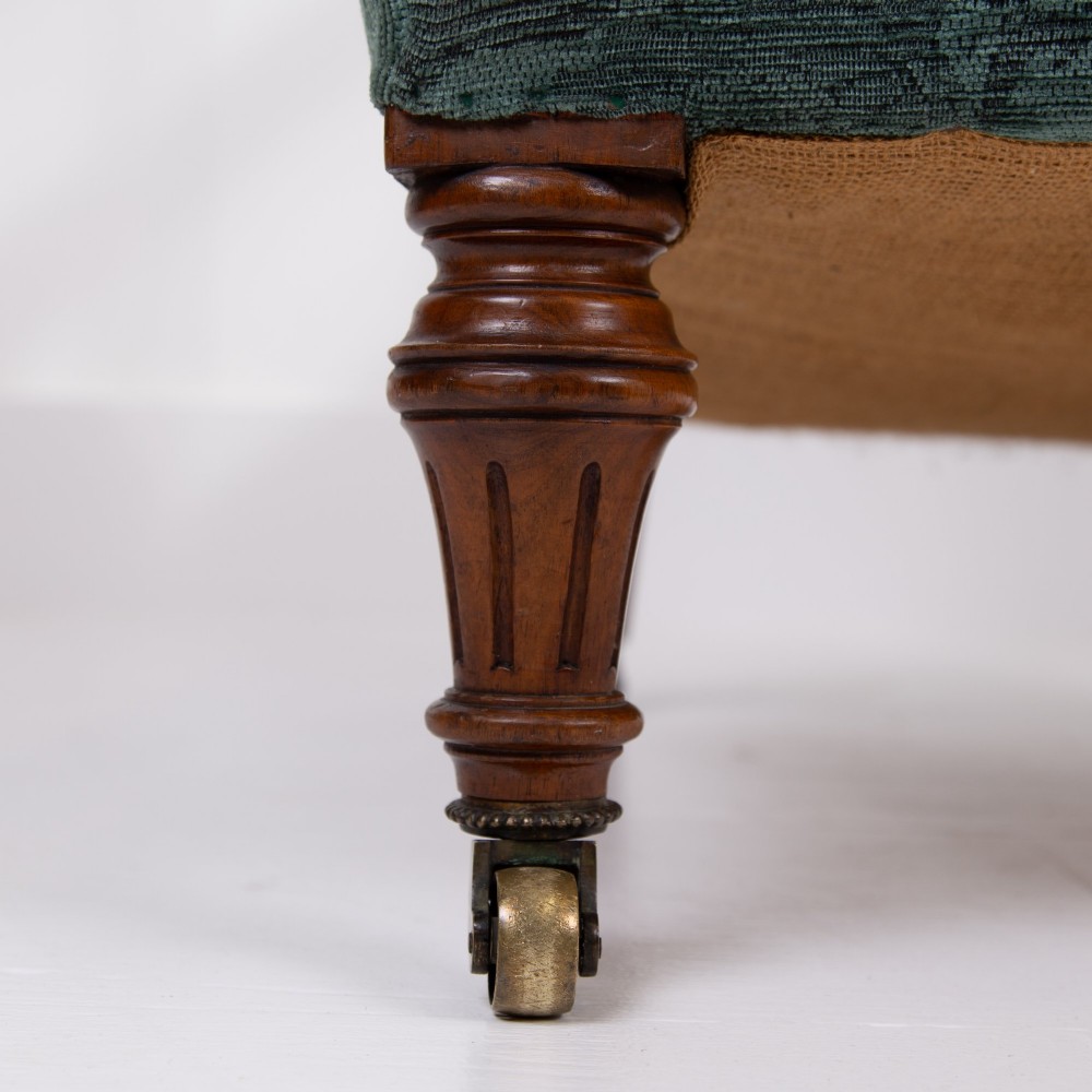 A profile view of a Victorian walnut open library armchair with dark green button-backed upholstery, turned front legs, and brass castors. View V