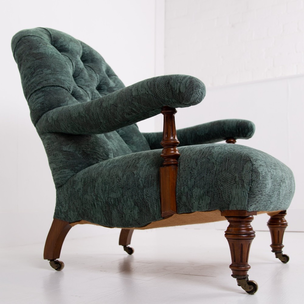 A profile view of a Victorian walnut open library armchair with dark green button-backed upholstery, turned front legs, and brass castors. View VI