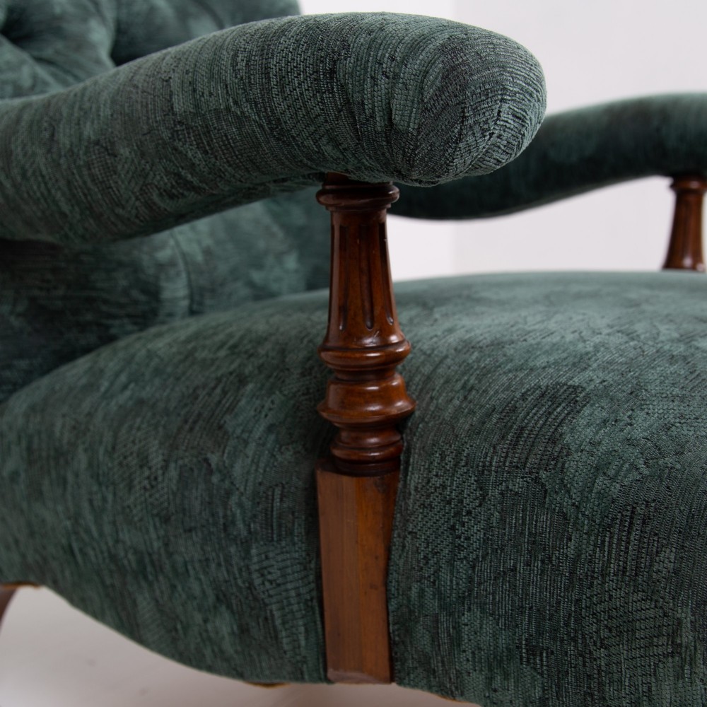 A profile view of a Victorian walnut open library armchair with dark green button-backed upholstery, turned front legs, and brass castors. View VII