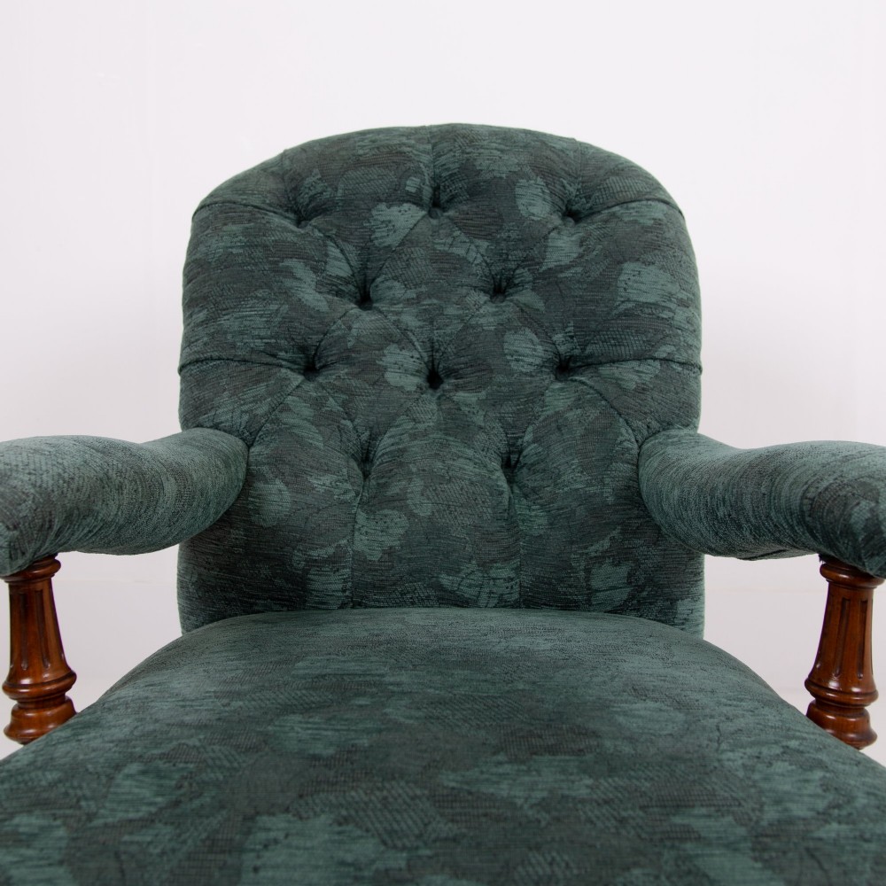 A profile view of a Victorian walnut open library armchair with dark green button-backed upholstery, turned front legs, and brass castors. View VIII