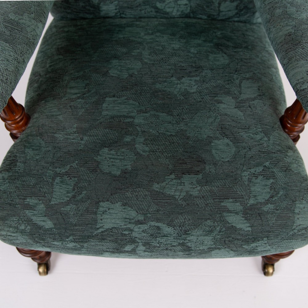 A profile view of a Victorian walnut open library armchair with dark green button-backed upholstery, turned front legs, and brass castors. View XI