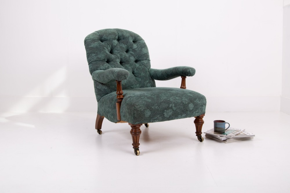 A profile view of a Victorian walnut open library armchair with dark green button-backed upholstery, turned front legs, and brass castors. View XIII