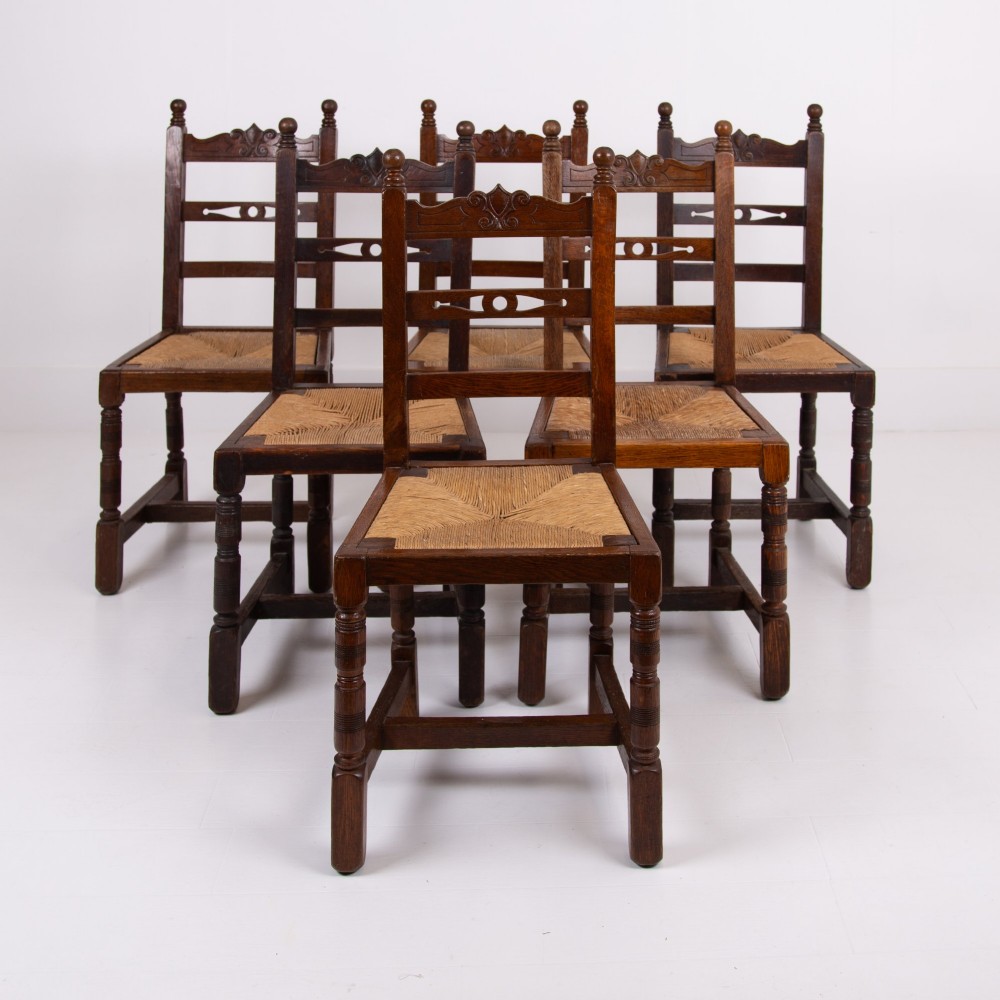A set of six dark oak country dining chairs featuring hand-woven rush seats, carved top rails, and turned front legs.