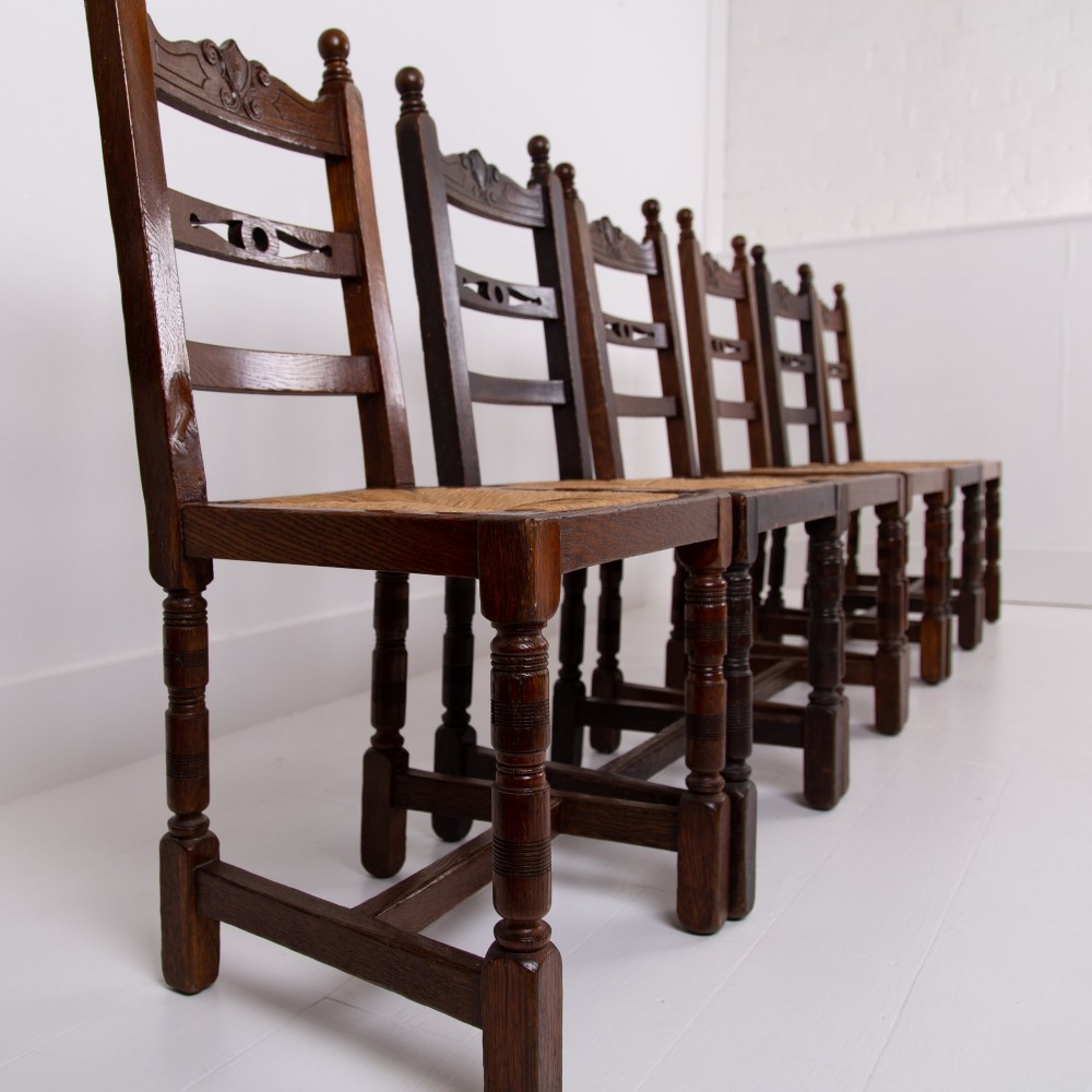 A set of six dark oak country dining chairs featuring hand-woven rush seats, carved top rails, and turned front legs. View II