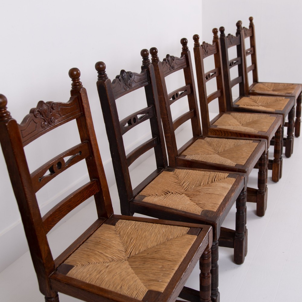 A set of six dark oak country dining chairs featuring hand-woven rush seats, carved top rails, and turned front legs. View III