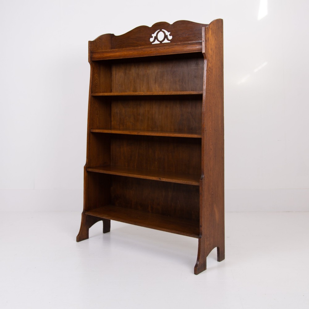 An Arts and Crafts solid oak open bookcase featuring five shelves, shaped side panels, and a decorative cresting rail with a pierced central cutout.