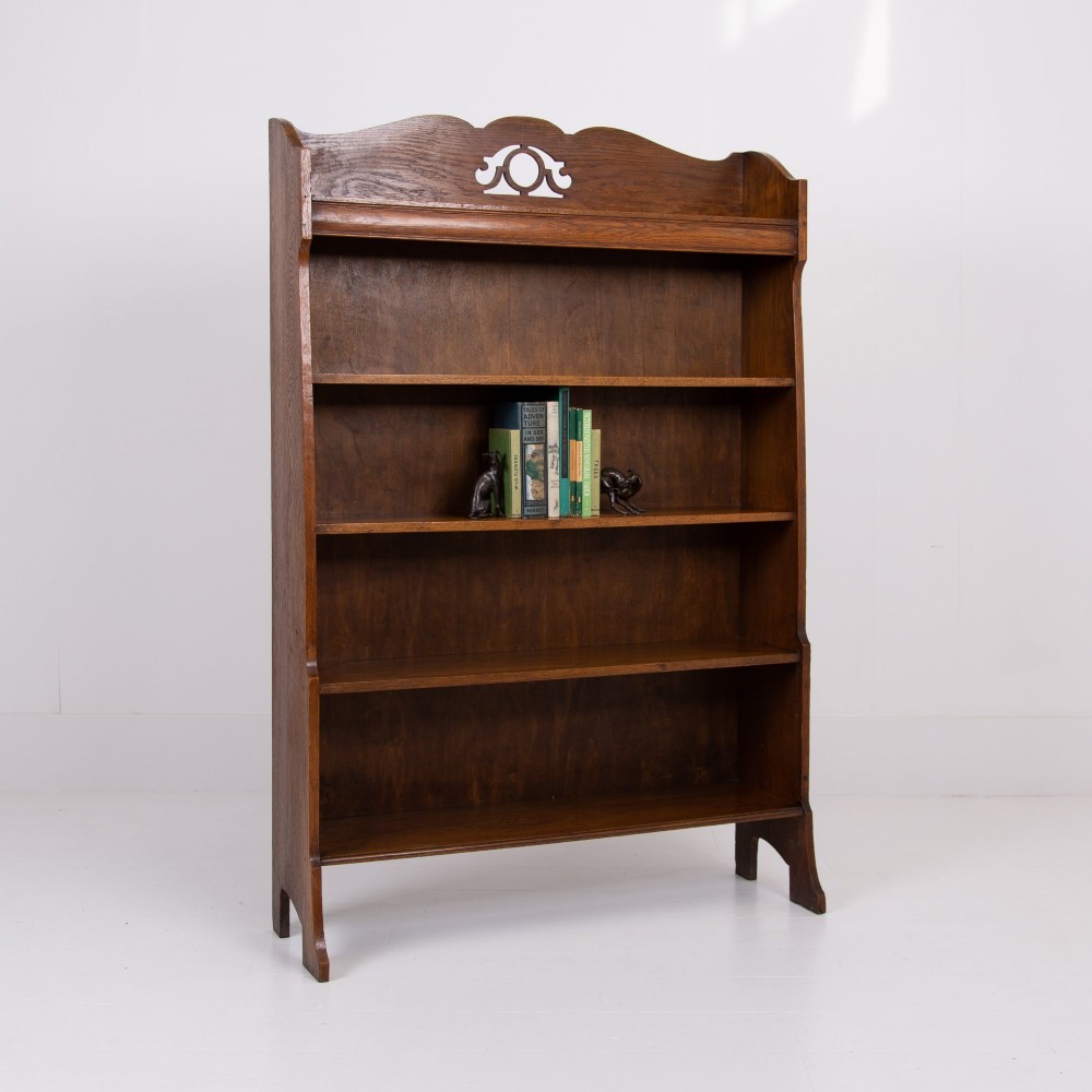 An Arts and Crafts solid oak open bookcase featuring five shelves, shaped side panels, and a decorative cresting rail with a pierced central cutout. View II