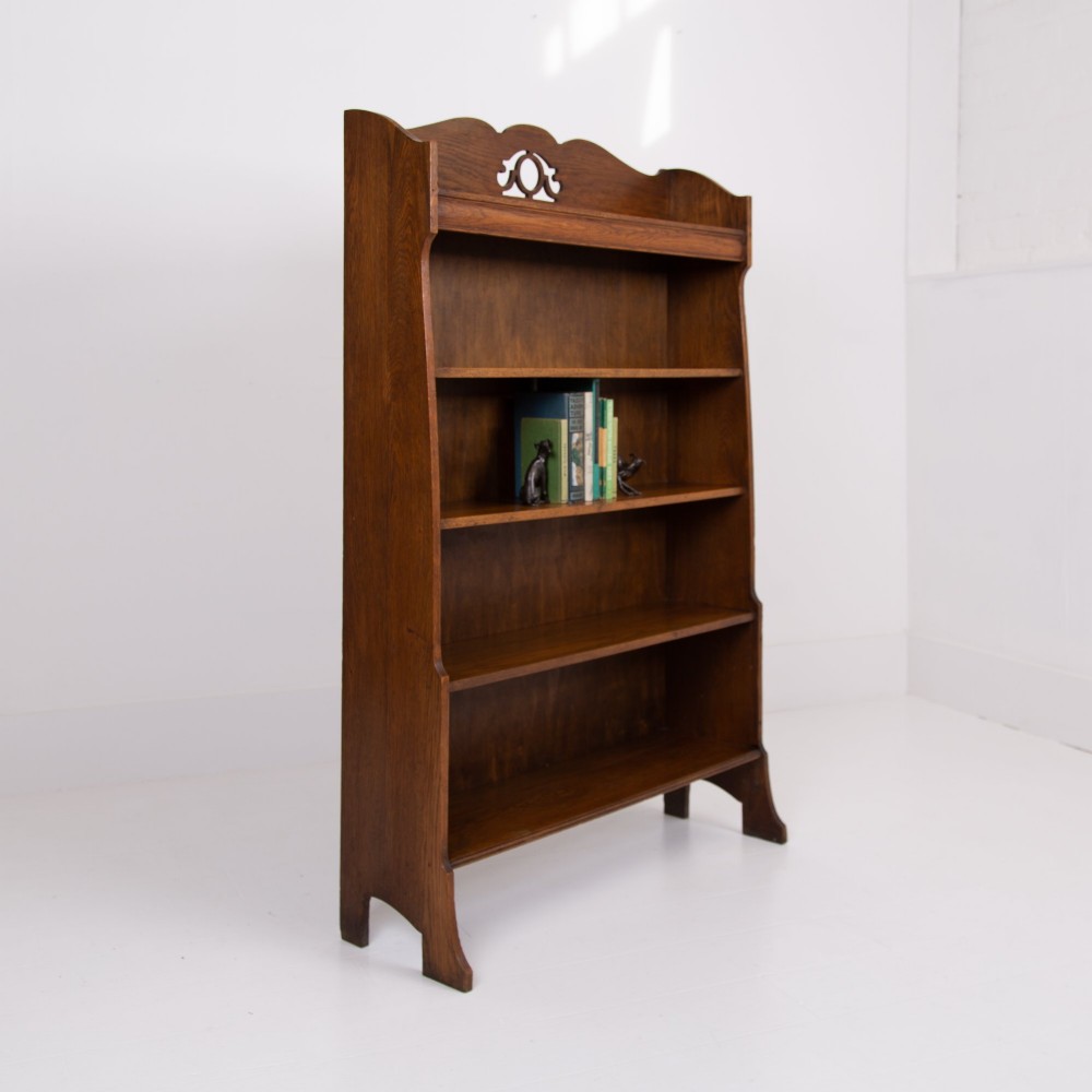 An Arts and Crafts solid oak open bookcase featuring five shelves, shaped side panels, and a decorative cresting rail with a pierced central cutout. View IV