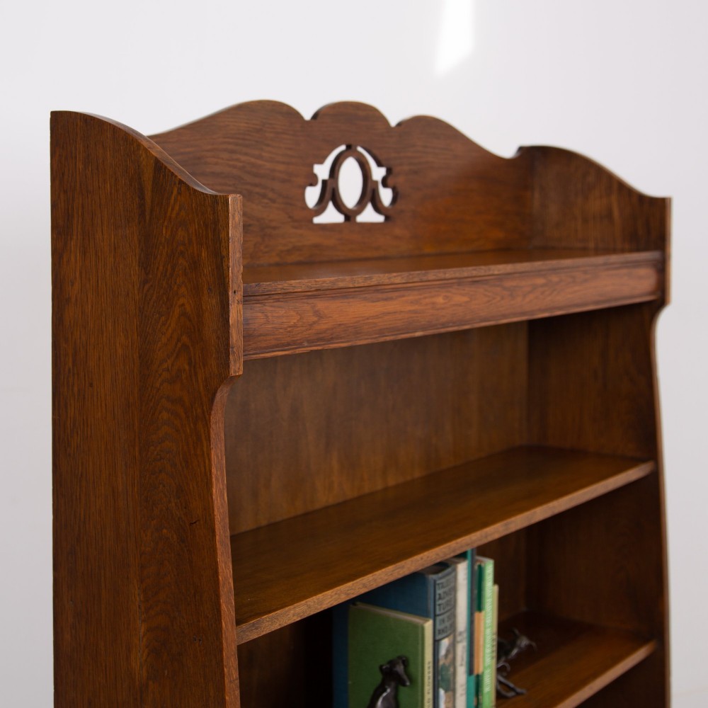 An Arts and Crafts solid oak open bookcase featuring five shelves, shaped side panels, and a decorative cresting rail with a pierced central cutout. View V