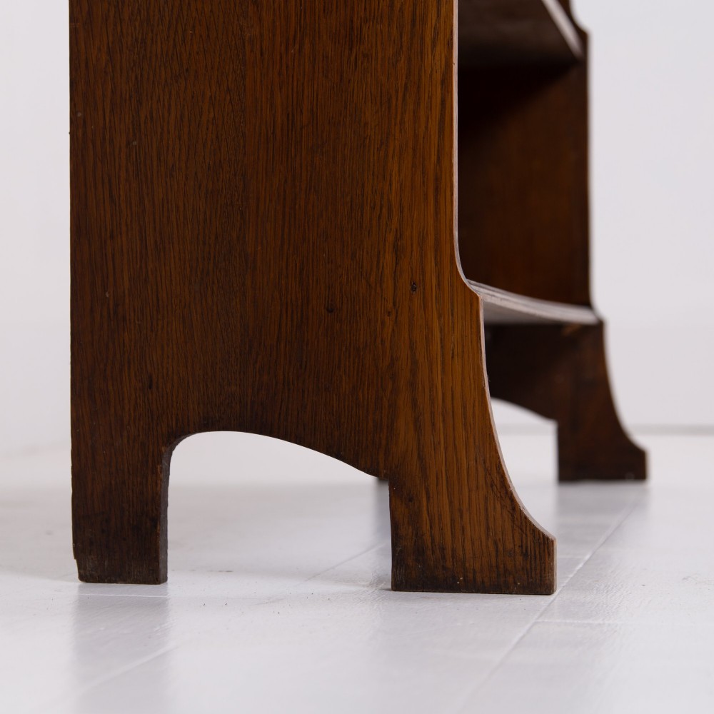An Arts and Crafts solid oak open bookcase featuring five shelves, shaped side panels, and a decorative cresting rail with a pierced central cutout. View VI