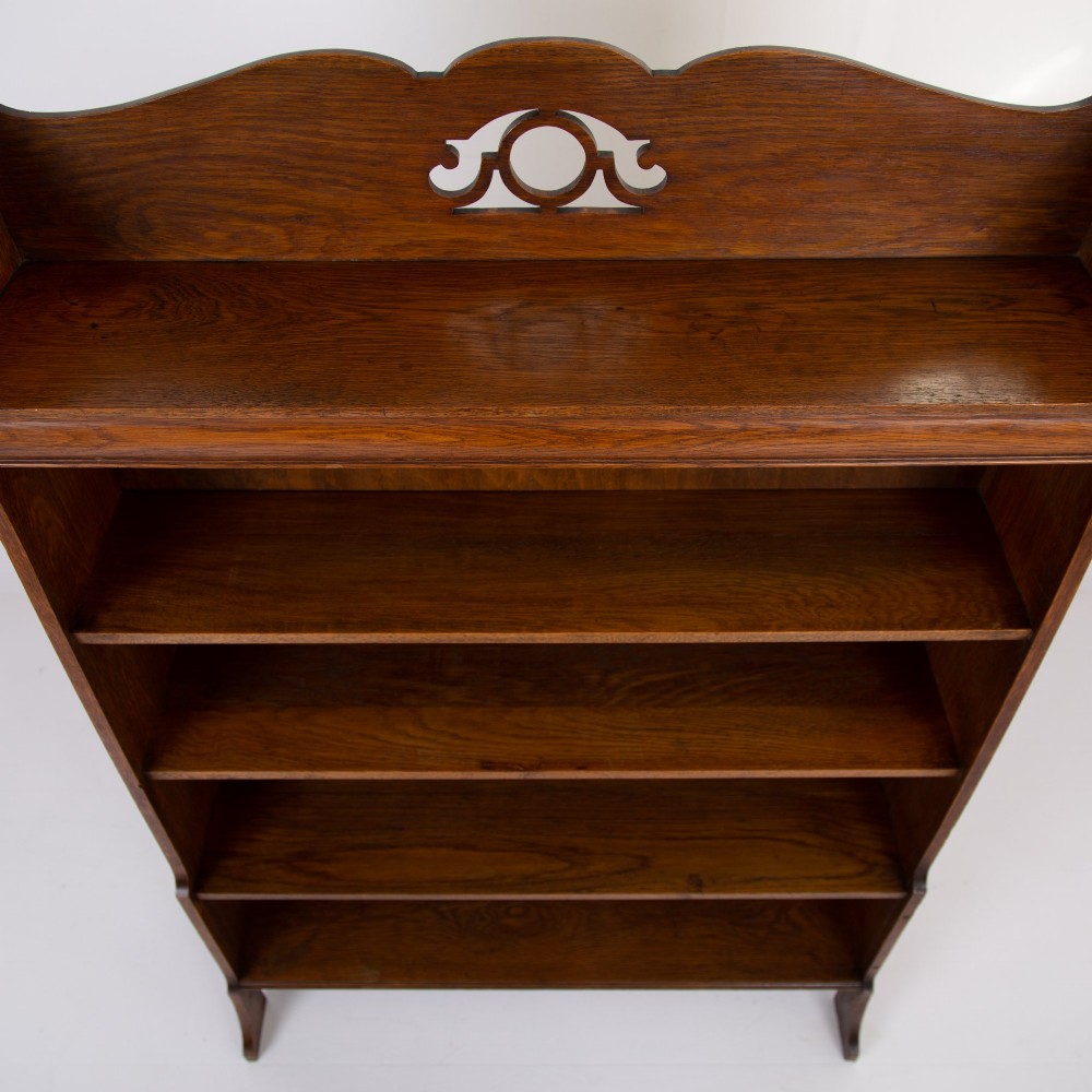 An Arts and Crafts solid oak open bookcase featuring five shelves, shaped side panels, and a decorative cresting rail with a pierced central cutout. View VIII