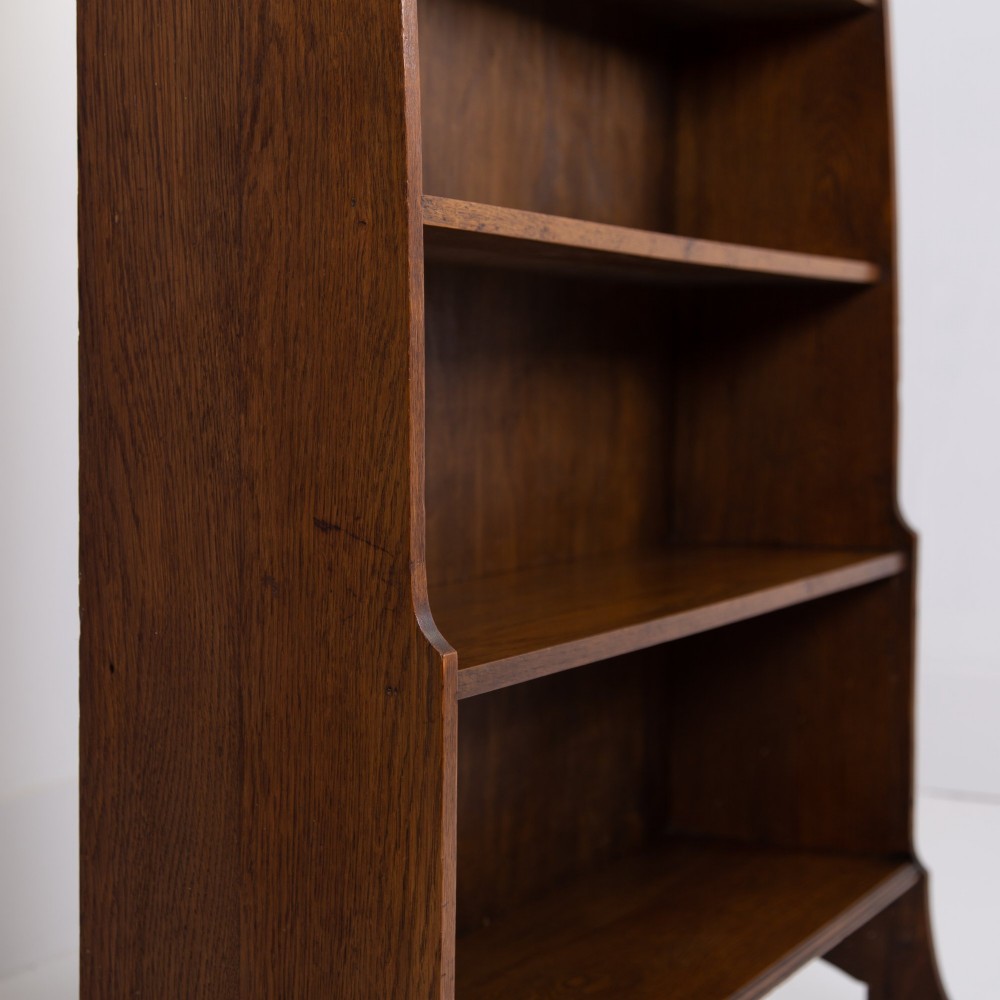 An Arts and Crafts solid oak open bookcase featuring five shelves, shaped side panels, and a decorative cresting rail with a pierced central cutout. View IX
