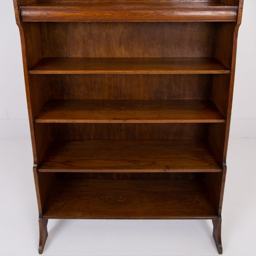 An Arts and Crafts solid oak open bookcase featuring five shelves, shaped side panels, and a decorative cresting rail with a pierced central cutout. View X
