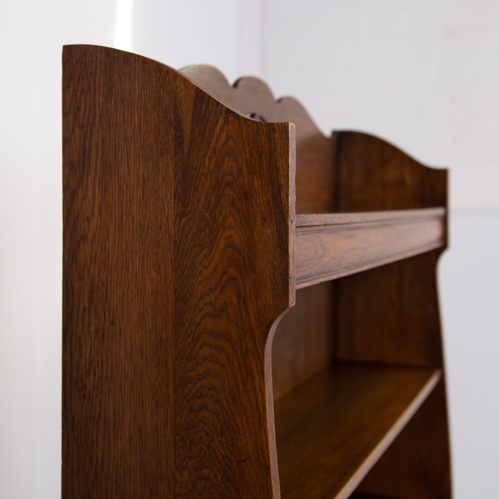 An Arts and Crafts solid oak open bookcase featuring five shelves, shaped side panels, and a decorative cresting rail with a pierced central cutout. View XI