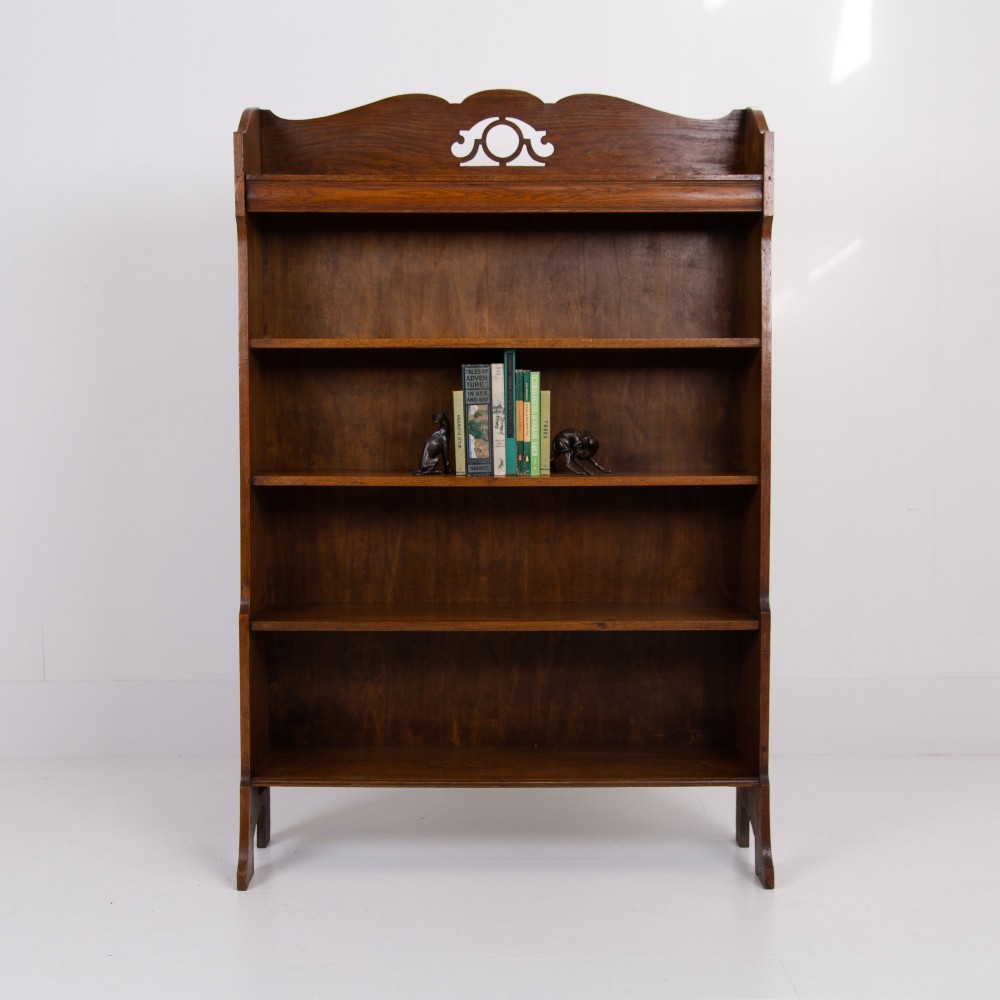 An Arts and Crafts solid oak open bookcase featuring five shelves, shaped side panels, and a decorative cresting rail with a pierced central cutout. View XIII