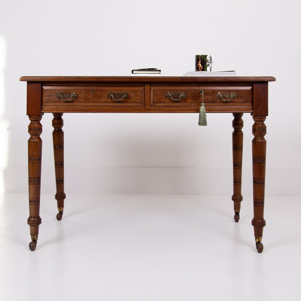 A late 19th-century walnut writing desk featuring two drawers with brass handles, turned legs on castors, and an inset leather top. View II