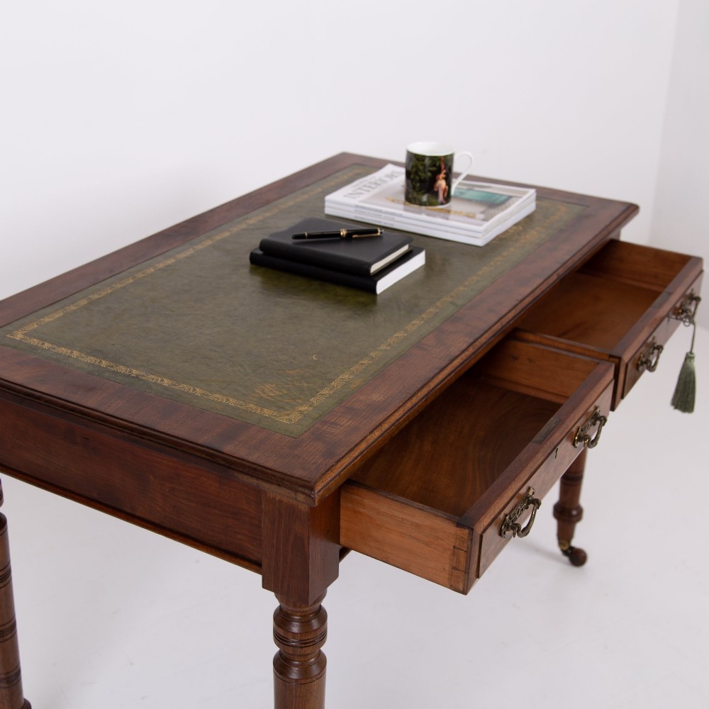 A late 19th-century walnut writing desk featuring two drawers with brass handles, turned legs on castors, and an inset leather top. View III