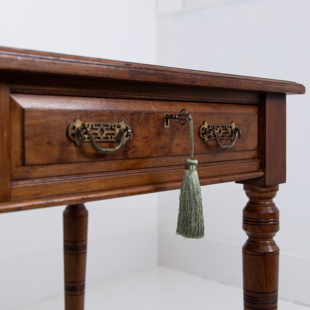 A late 19th-century walnut writing desk featuring two drawers with brass handles, turned legs on castors, and an inset leather top. View V