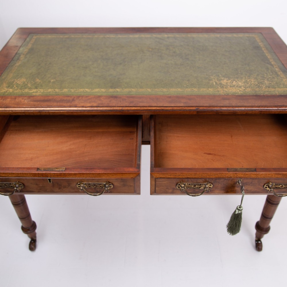 A late 19th-century walnut writing desk featuring two drawers with brass handles, turned legs on castors, and an inset leather top. View VII