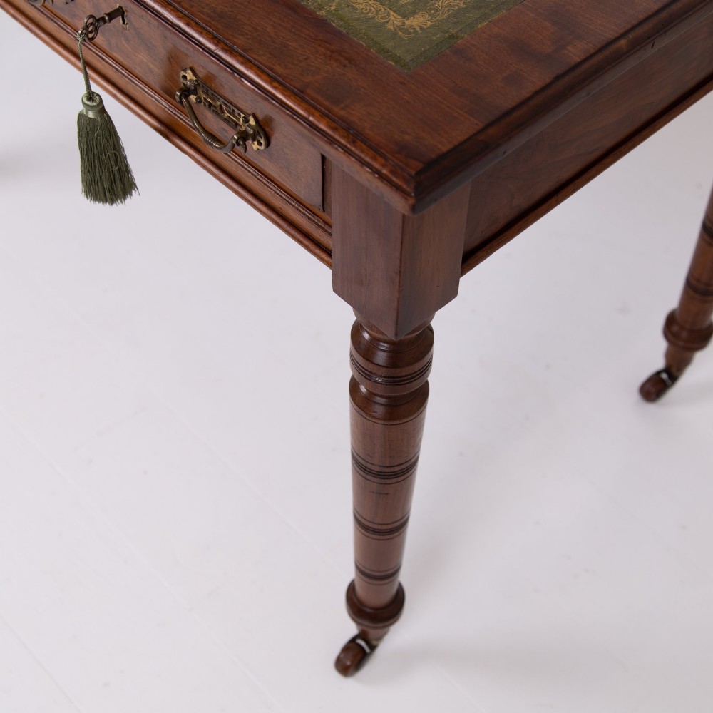 A late 19th-century walnut writing desk featuring two drawers with brass handles, turned legs on castors, and an inset leather top. View XI
