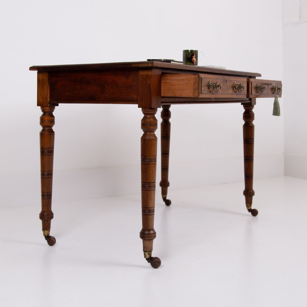 A late 19th-century walnut writing desk featuring two drawers with brass handles, turned legs on castors, and an inset leather top. View XII
