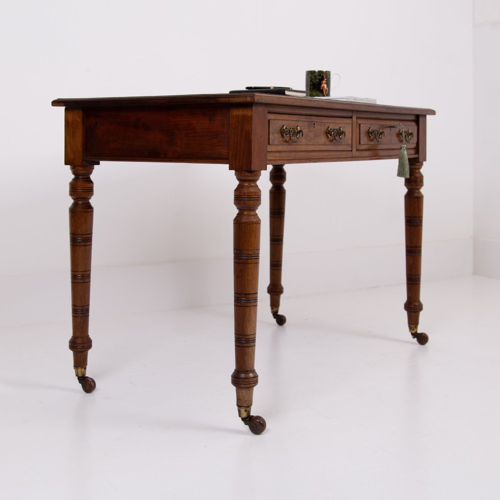 A late 19th-century walnut writing desk featuring two drawers with brass handles, turned legs on castors, and an inset leather top. View XIII