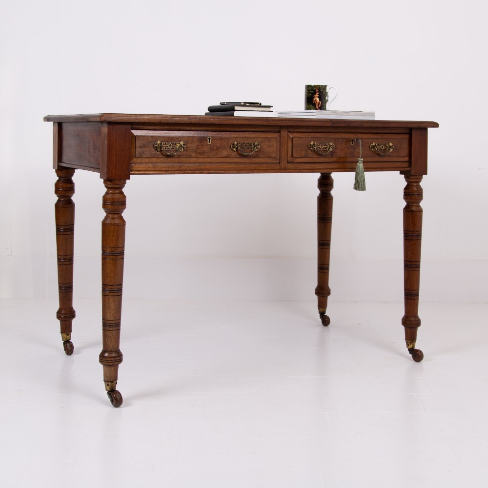 A late 19th-century walnut writing desk featuring two drawers with brass handles, turned legs on castors, and an inset leather top. View XIV