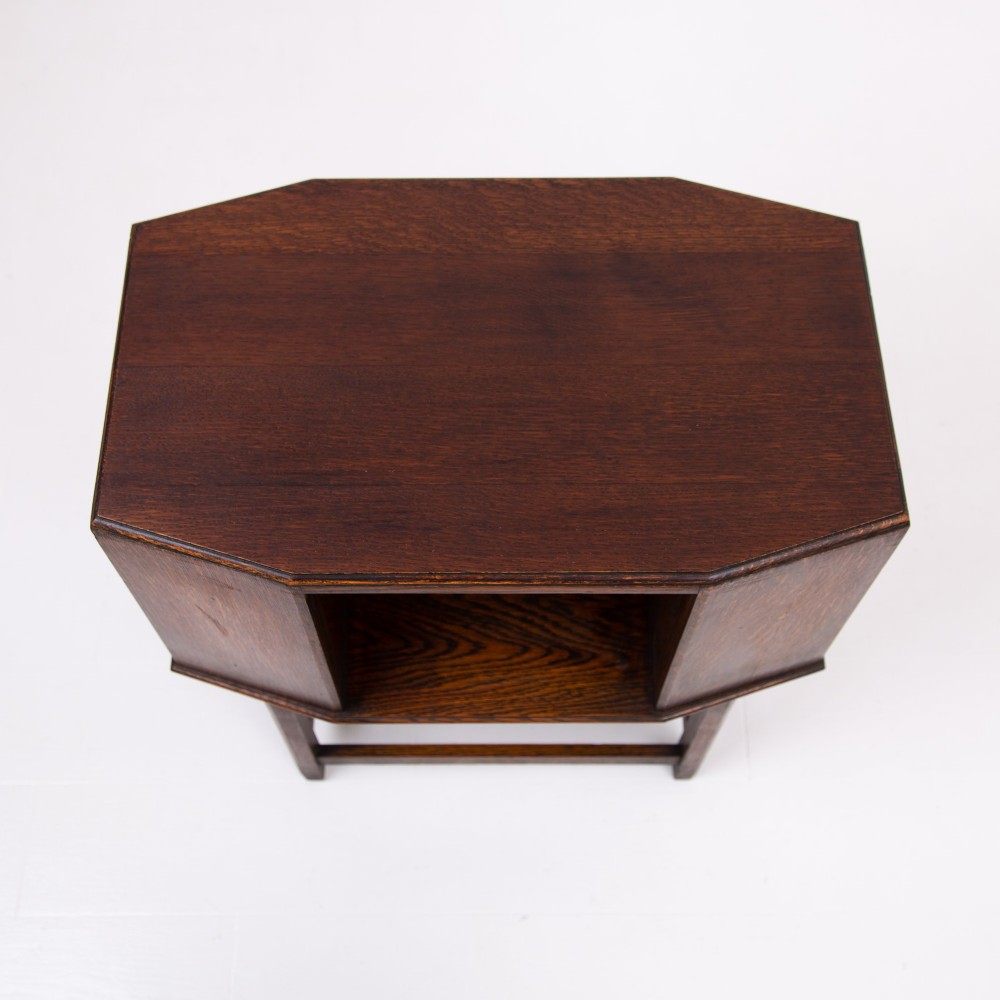 An Art Deco dark oak side table featuring an octagonal top, open central niche, side book compartments, and straight legs with square stretchers. View V