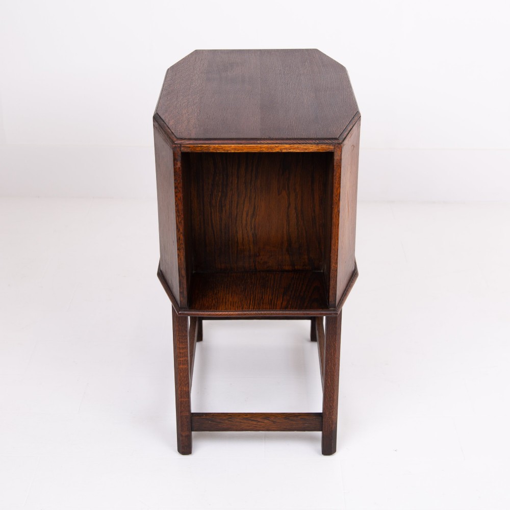 An Art Deco dark oak side table featuring an octagonal top, open central niche, side book compartments, and straight legs with square stretchers. View VI