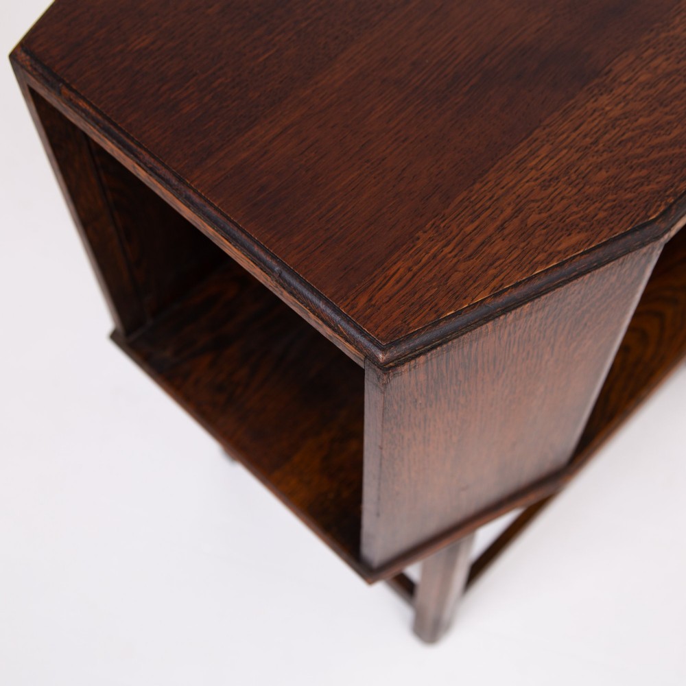 An Art Deco dark oak side table featuring an octagonal top, open central niche, side book compartments, and straight legs with square stretchers. View X