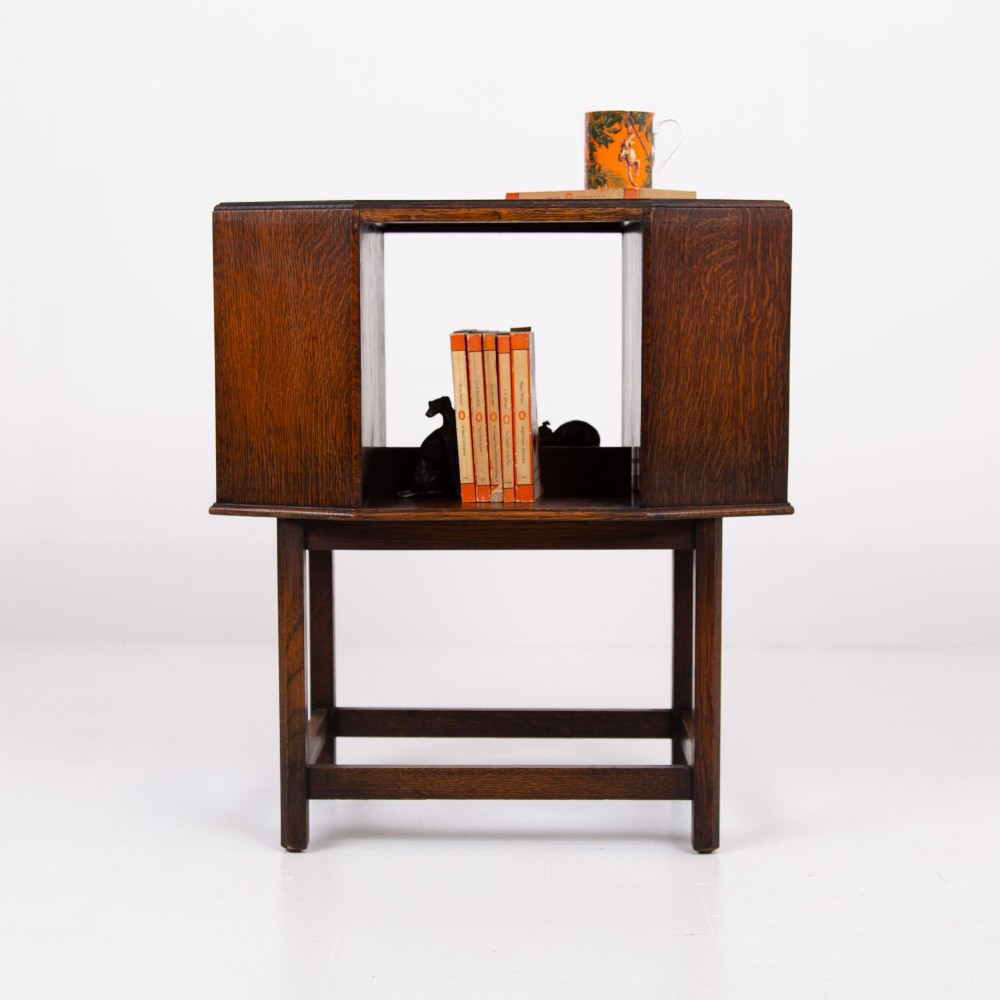 An Art Deco dark oak side table featuring an octagonal top, open central niche, side book compartments, and straight legs with square stretchers. View XI