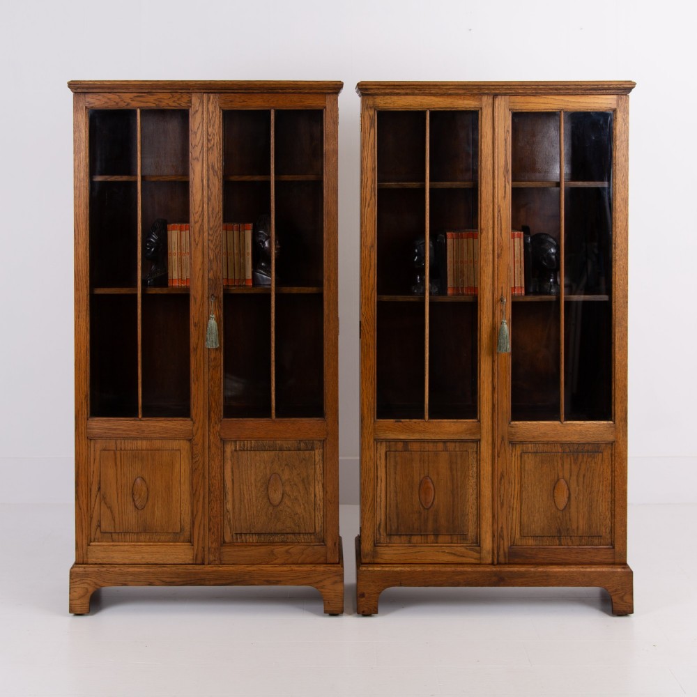 A matching pair of 1930s solid English oak bookcases featuring glazed twin doors above oval-carved lower door panels.