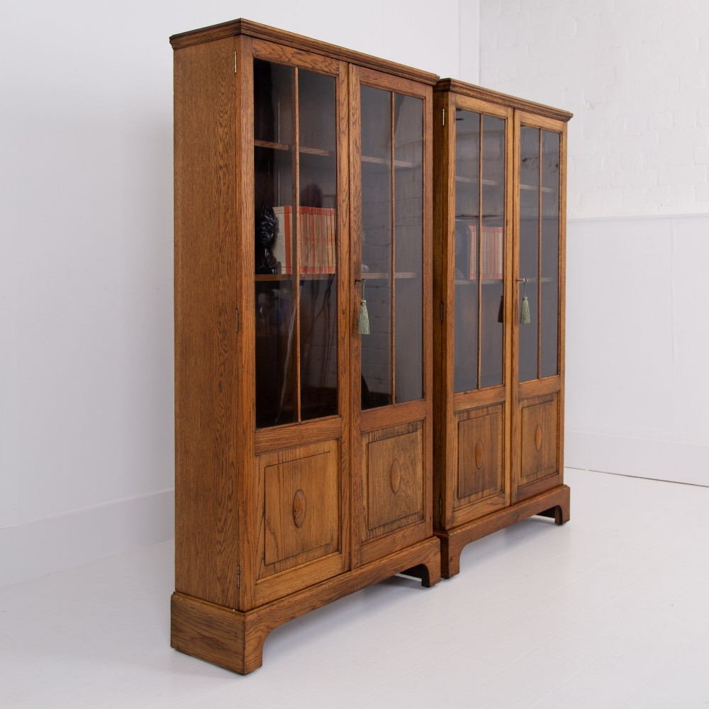 A matching pair of 1930s solid English oak bookcases featuring glazed twin doors above oval-carved lower door panels. View II