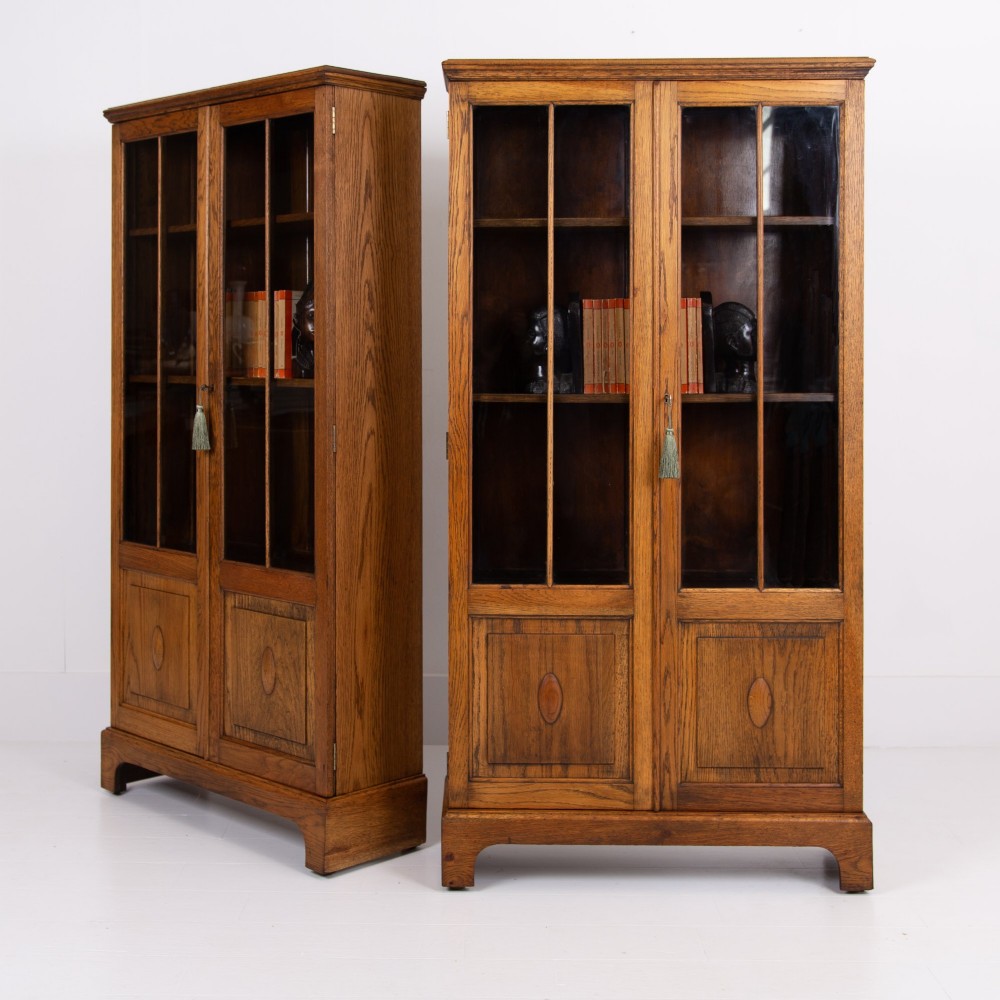 A matching pair of 1930s solid English oak bookcases featuring glazed twin doors above oval-carved lower door panels. View VII