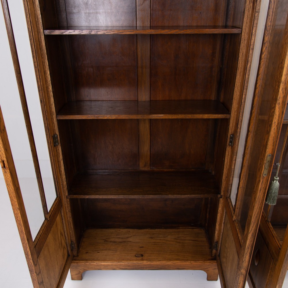A matching pair of 1930s solid English oak bookcases featuring glazed twin doors above oval-carved lower door panels. View IX