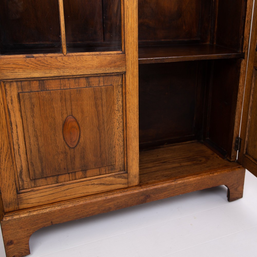 A matching pair of 1930s solid English oak bookcases featuring glazed twin doors above oval-carved lower door panels. View X