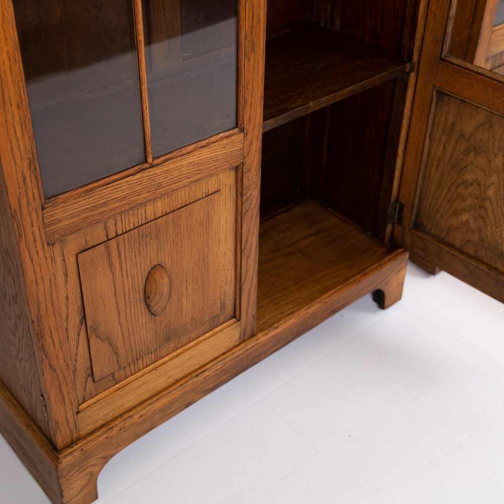 A matching pair of 1930s solid English oak bookcases featuring glazed twin doors above oval-carved lower door panels. View XI