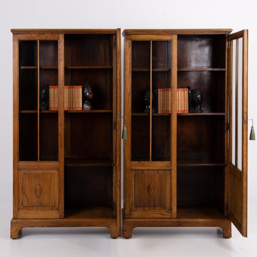 A matching pair of 1930s solid English oak bookcases featuring glazed twin doors above oval-carved lower door panels. View XIV