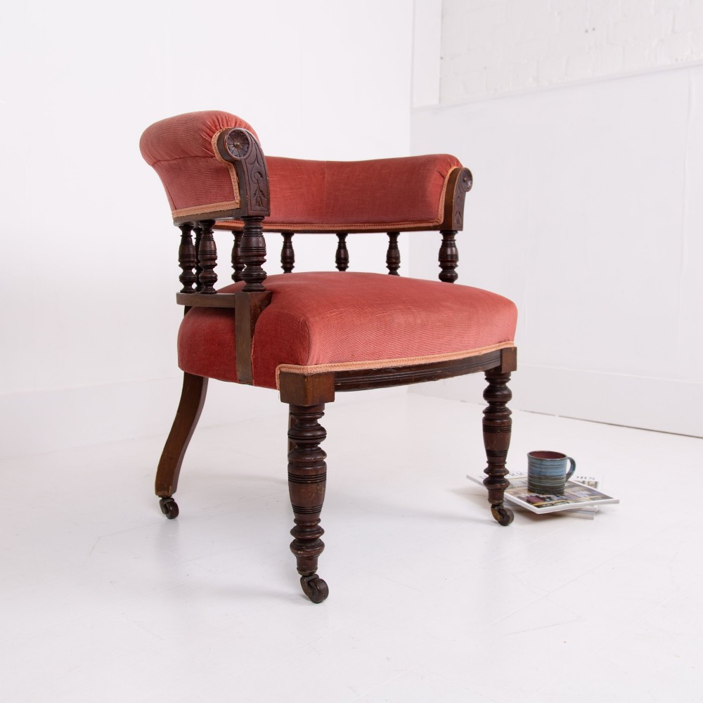 A late Victorian armchair featuring a curved horseshoe back rest, turned wood spindles, terracotta fabric upholstery, and turned front legs on castors. View III