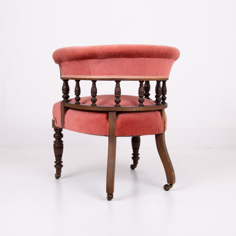 A late Victorian armchair featuring a curved horseshoe back rest, turned wood spindles, terracotta fabric upholstery, and turned front legs on castors. View IV